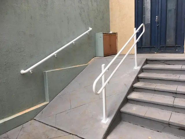 Corrimão branco acompanhando os degraus de uma escada externa até a porta de entrada