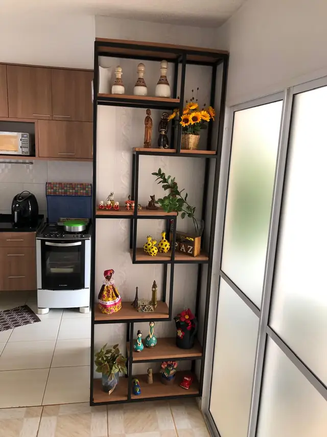 Estante de estrutura metálica preta com prateleiras de madeira em alturas alternadas, montada entre a cozinha e a sala
