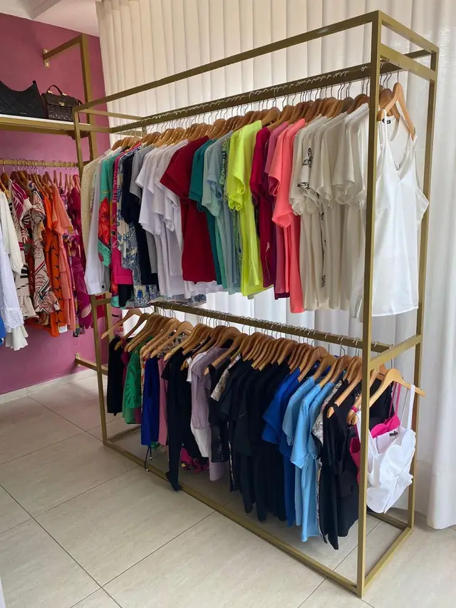 Arara metálica dourada com roupas penduradas, numa loja de roupas
