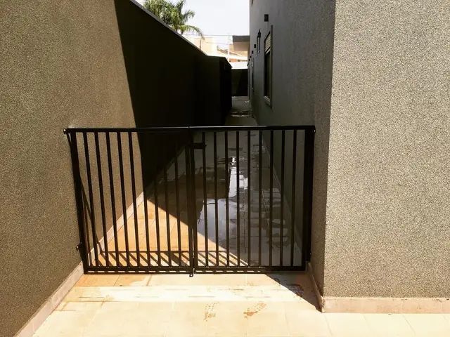 Portão de barras verticais pretas fechando a passagem lateral entre duas casas