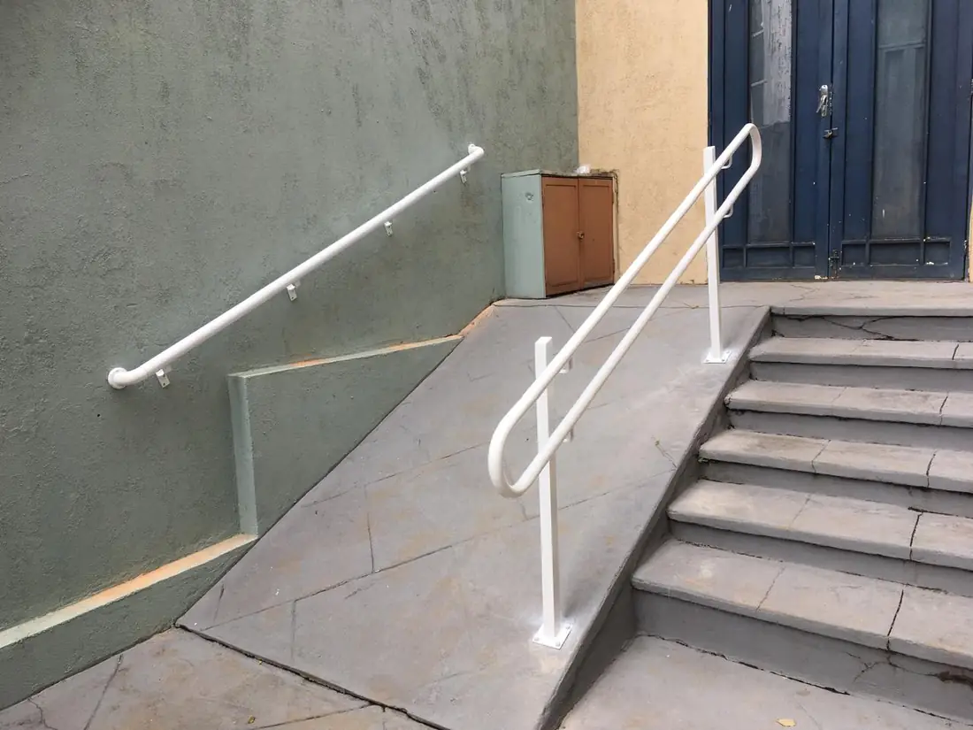 Corrimão branco acompanhando os degraus de uma escada externa até a porta de entrada