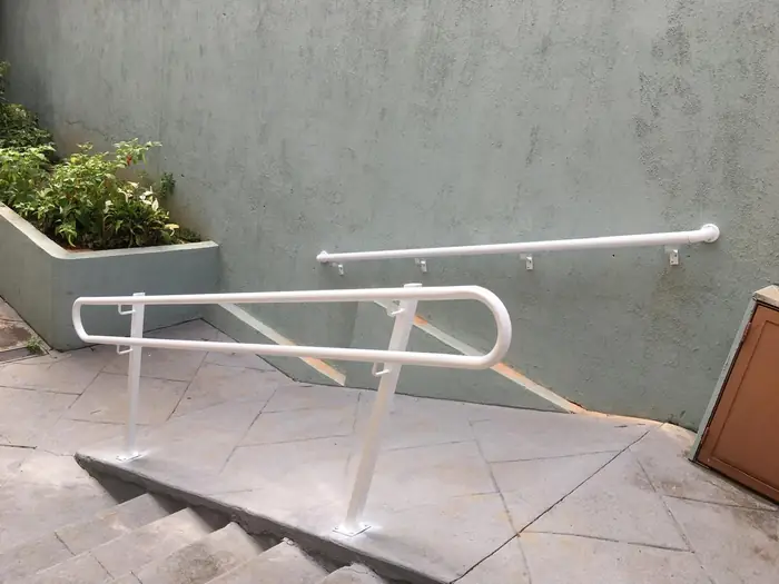 O mesmo corrimão branco visto do alto da escada, contornando o canteiro