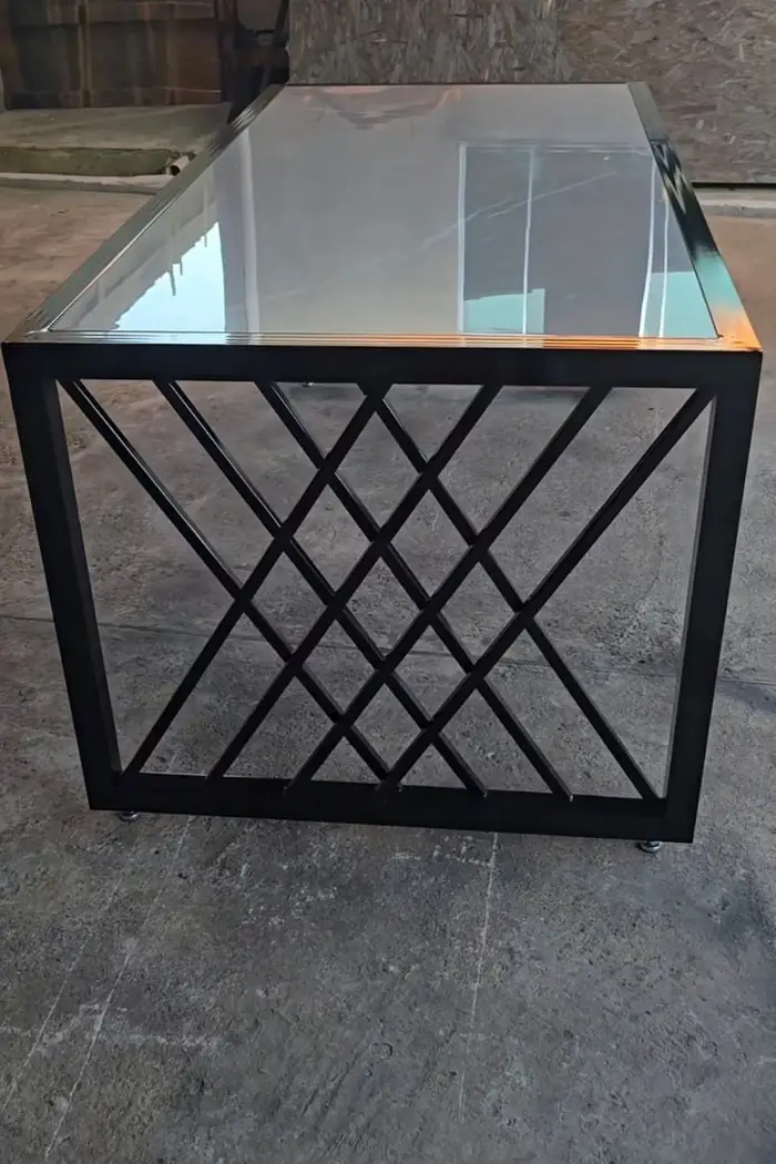 Mesa de base metálica preta em treliça cruzada, com tampo de vidro, ao ar livre