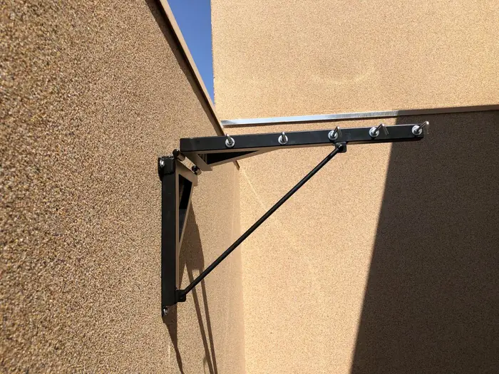 O suporte do varal visto de frente na parede, com a sombra projetada no reboco